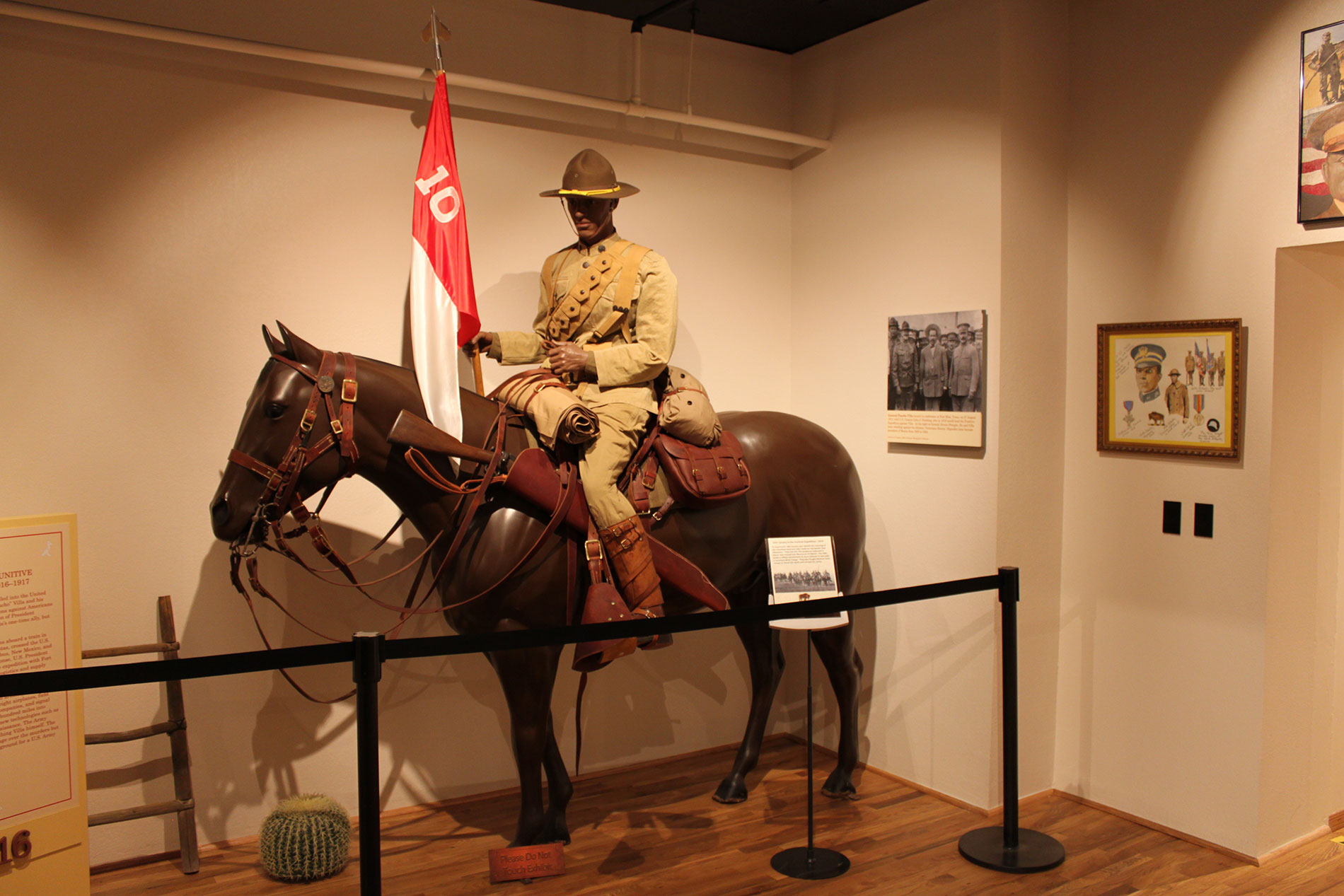 Museum exhibit of a Soldier riding a brown horse carrying a flag.